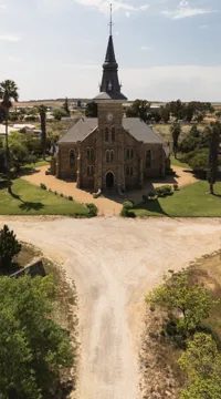 A church with a tall spire at the end of a tree-lined road, seen from the air